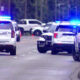 Several police SUVs with red and blue lights flashing on a suburban street, blocking traffic or securing a scene.