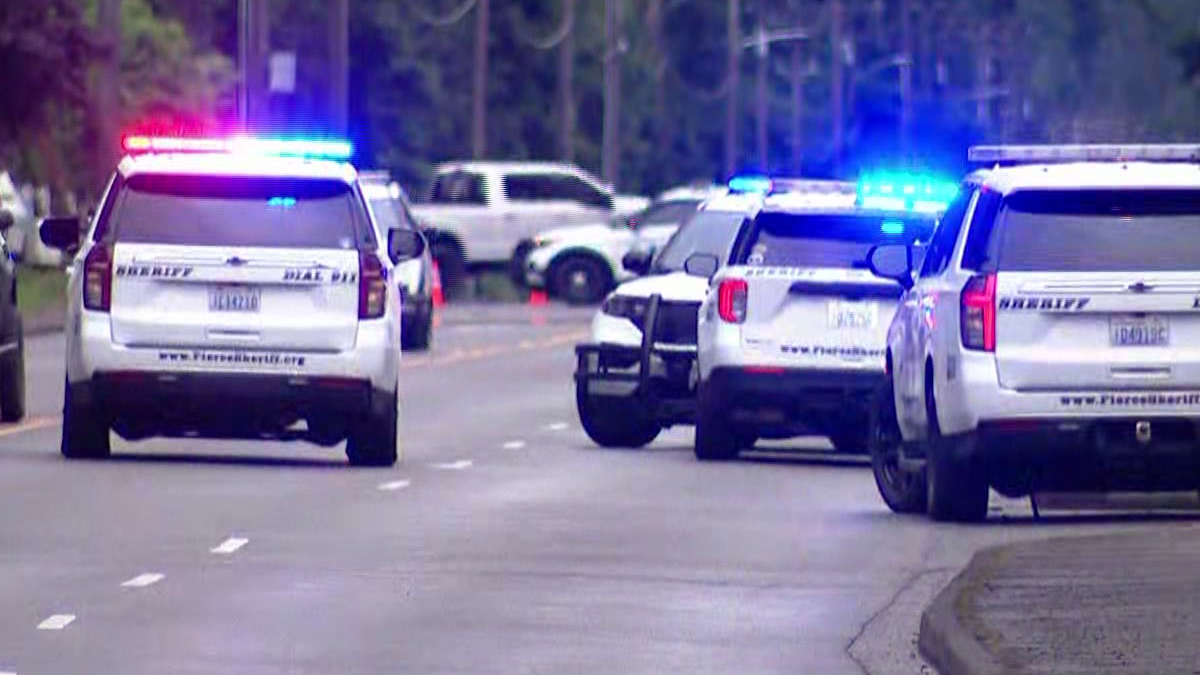 Several police SUVs with red and blue lights flashing on a suburban street, blocking traffic or securing a scene.