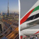 Dubai skyline at dusk with complex highway interchanges on the left; Emirates aircraft tails on the right.
