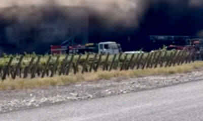 Emergency vehicles and a white van near a smoke-filled tunnel, seen from the roadside with a wooden fence in the foreground
