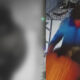 Surveillance still of a person in a blue jacket walking on a sidewalk, captured by a security camera on the right side of the frame.