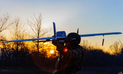 Soldier in tactical gear launching a small white drone airplane at sunset.