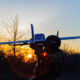 Soldier in tactical gear launching a small white drone airplane at sunset.