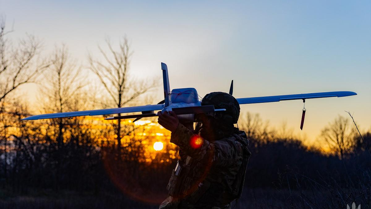 Soldier in tactical gear launching a small white drone airplane at sunset.