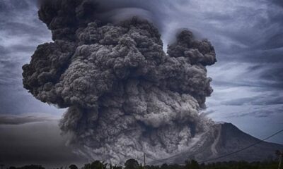 Volcanic eruption with a massive dark ash cloud rising from a mountain, billowing into the sky.