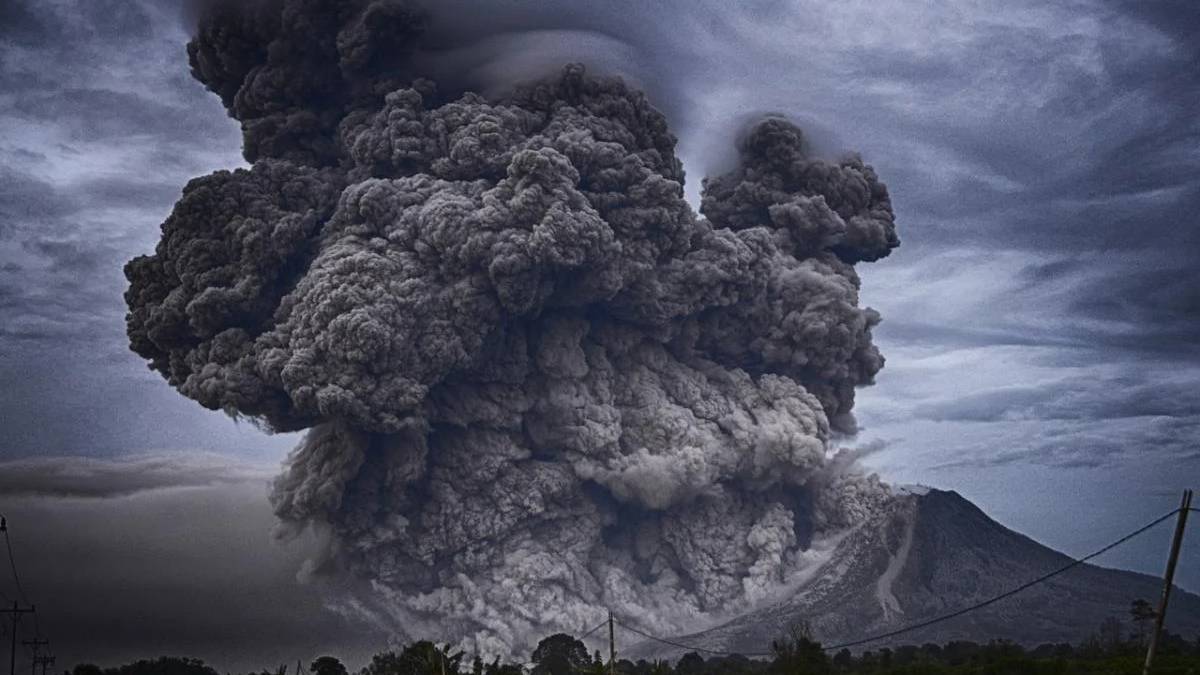Volcanic eruption with a massive dark ash cloud rising from a mountain, billowing into the sky.