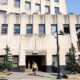Front entrance of a beige art-deco building labeled 'Tacoma Building' with a man in a safety vest walking by, on a city street.