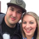 Smiling man and woman taking a selfie outdoors, facing the camera with heads close together.