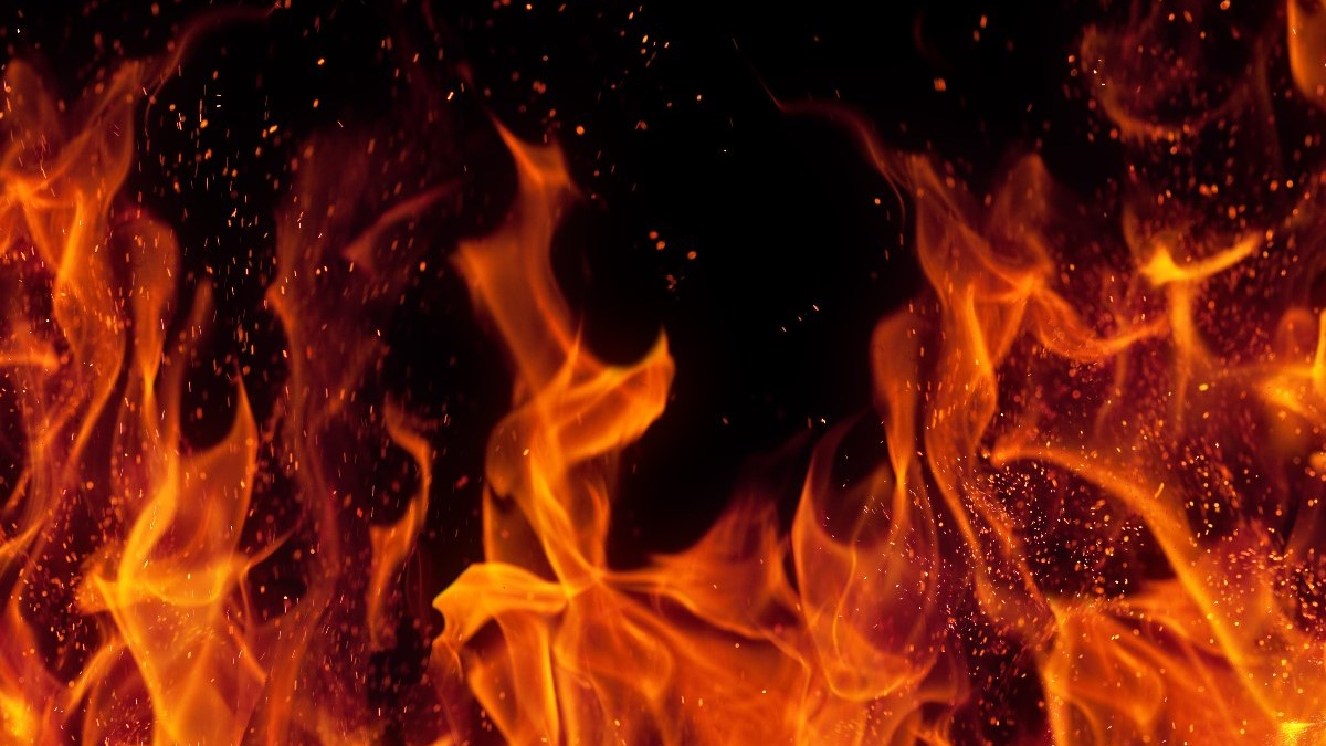 Close-up of bright orange flames and glowing embers against a dark background, conveying intense fire.