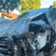 Blue SUV with severe front-end damage after a crash, parked on a curb with responders nearby on a residential street