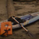 Inflatable kayak with a paddle and orange life jacket placed on a sandy beach, ready for paddling.