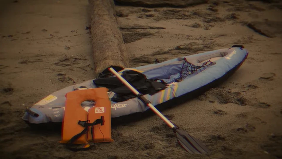 Inflatable kayak with a paddle and orange life jacket placed on a sandy beach, ready for paddling.