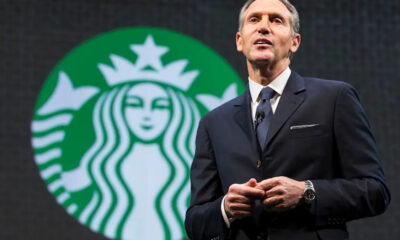 Man in a dark suit giving a speech on stage with a large Starbucks logo in the background behind him called to attention the brand scene behind him