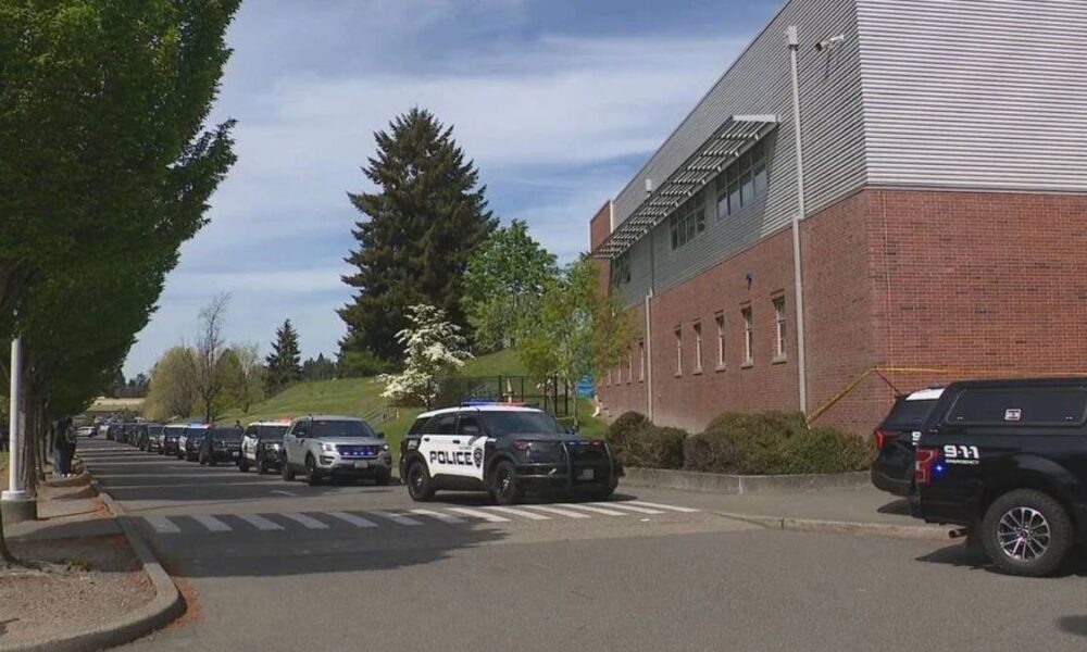 Line of police SUVs parked along a street beside a brick building, with trees and a crosswalk in the foreground.