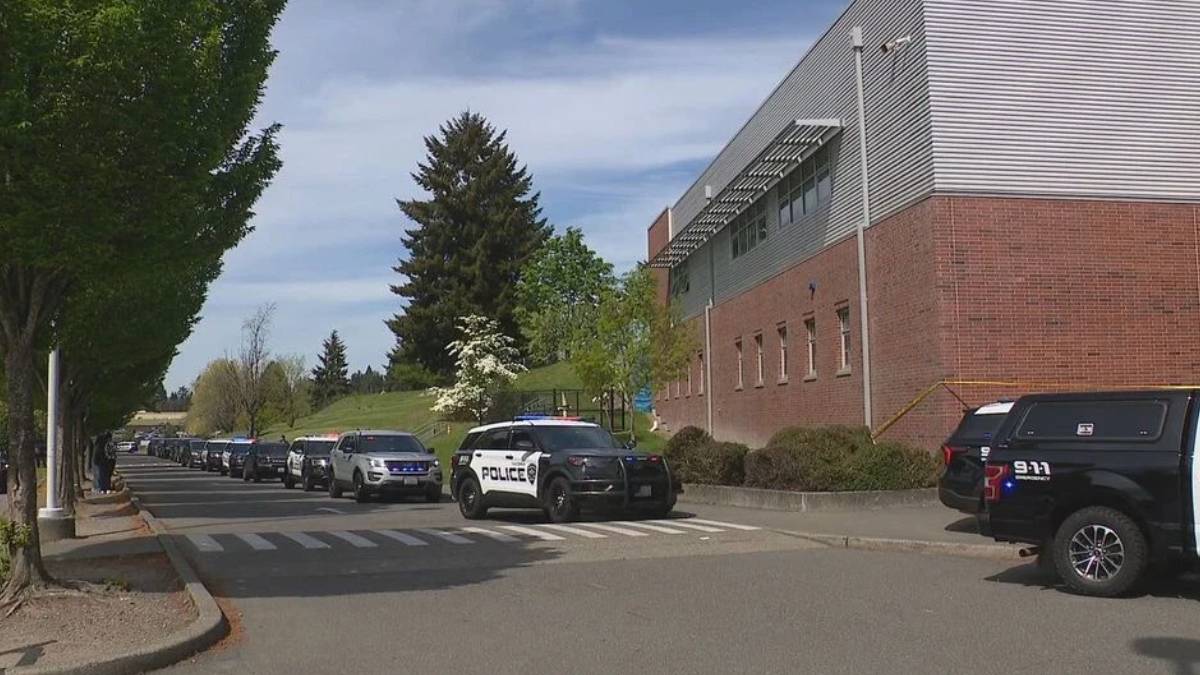 Line of police SUVs parked along a street beside a brick building, with trees and a crosswalk in the foreground.
