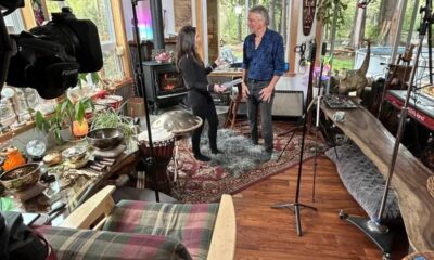 Two people converse in a cozy home studio filled with musical instruments and recording gear.