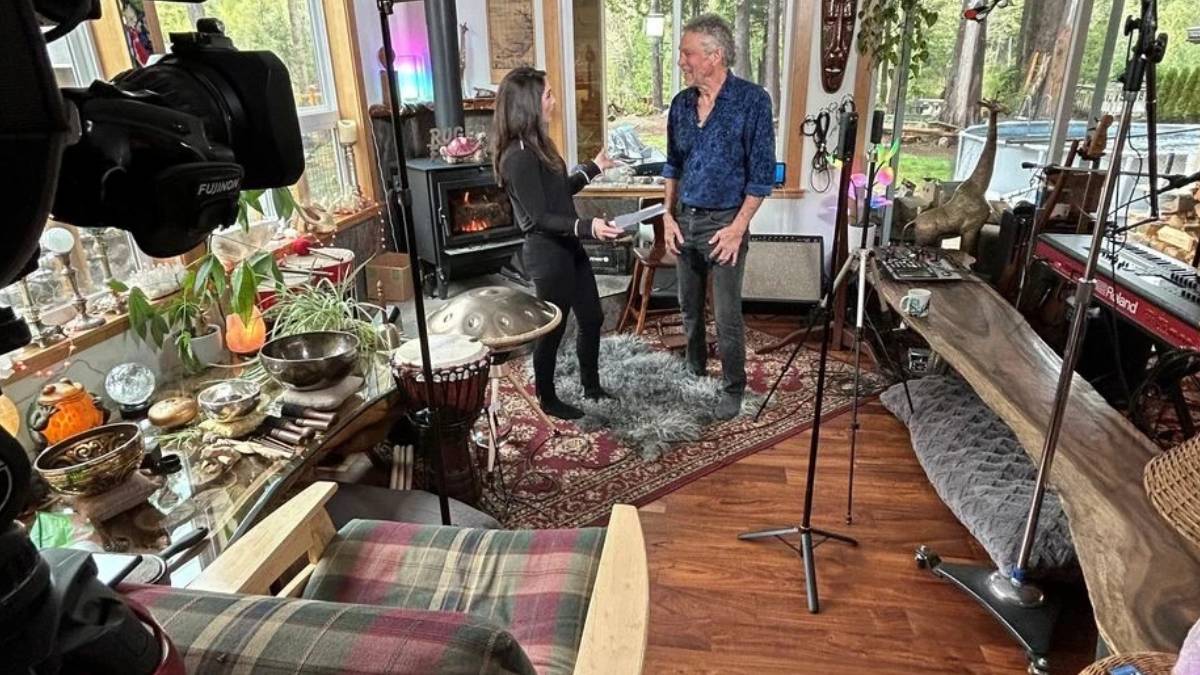 Two people converse in a cozy home studio filled with musical instruments and recording gear.