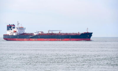 Large cargo ship sailing on calm sea under a pale sky, blue hull with red bottom edge.