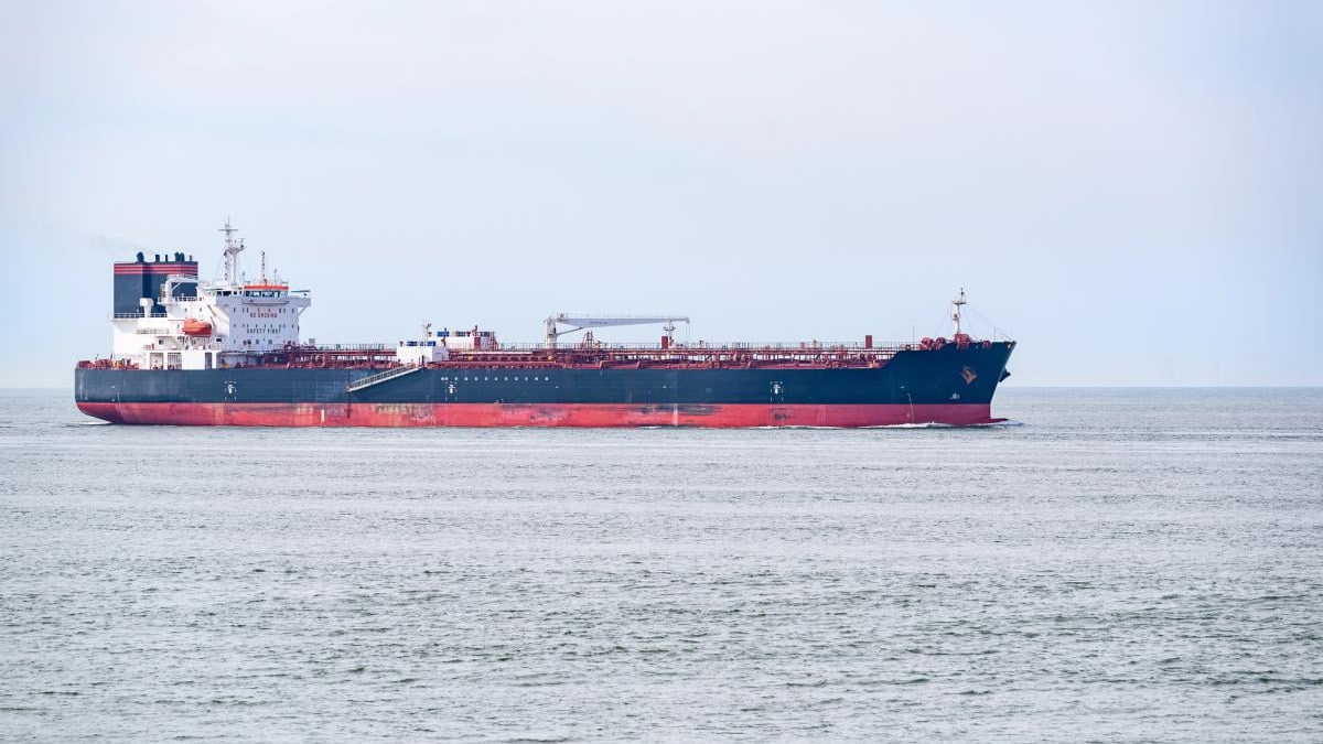 Large cargo ship sailing on calm sea under a pale sky, blue hull with red bottom edge.