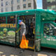 Green King County Metro waterfront shuttle bus with doors open, a man carrying an orange bag stepping onto the sidewalk.