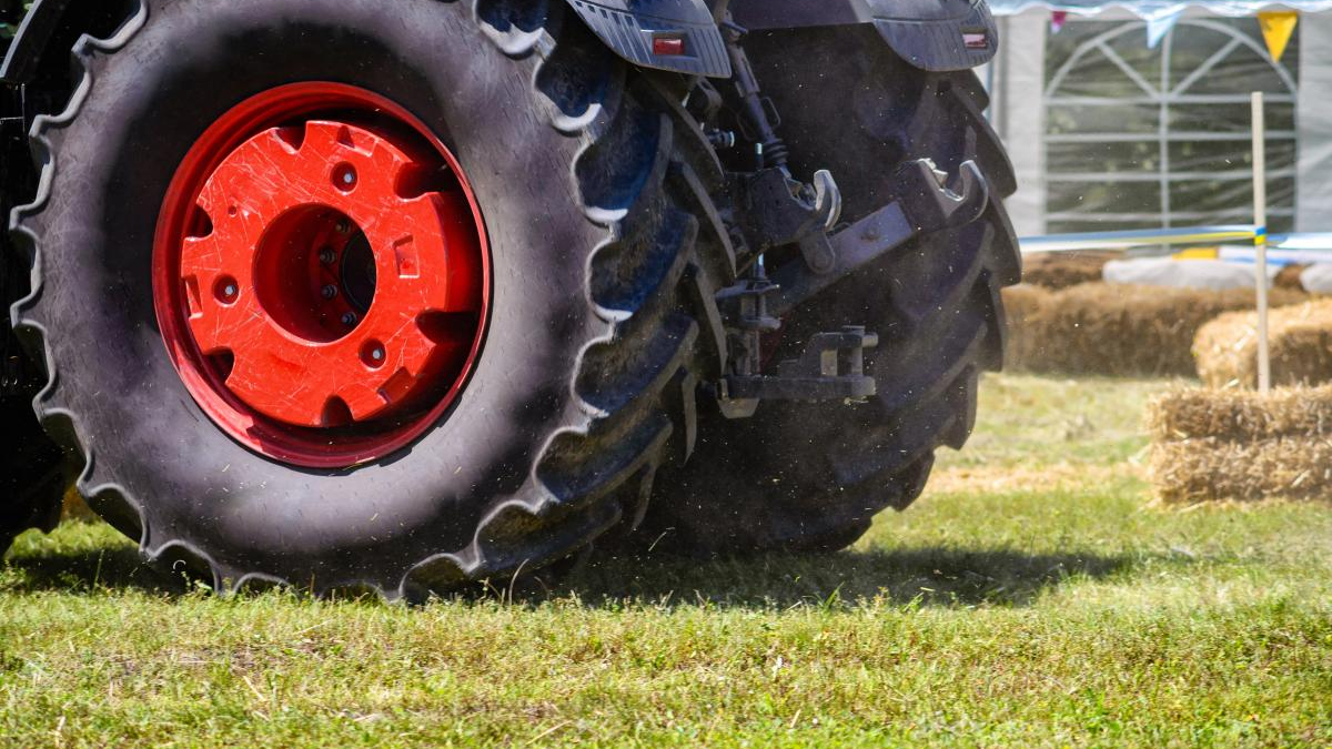 Close-up of a tractor wheel with a red rim on a grassy field at an outdoor event for an agricultural demonstration.