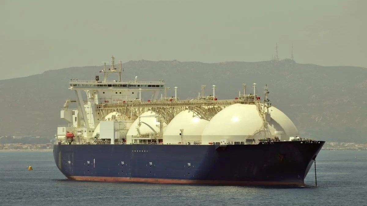 Large blue LNG carrier with three white spherical tanks on calm sea, hills in the background.
