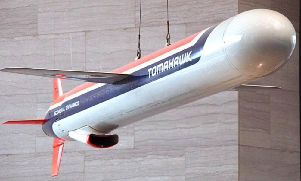 Hanging display model of a Tomahawk aircraft with red, white, and blue livery labeled Tomahawk and General Dynamics, suspended from cables against a stone wall