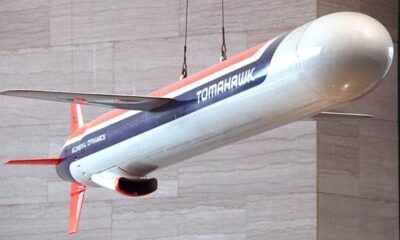 Hanging display model of a Tomahawk aircraft with red, white, and blue livery labeled Tomahawk and General Dynamics, suspended from cables against a stone wall
