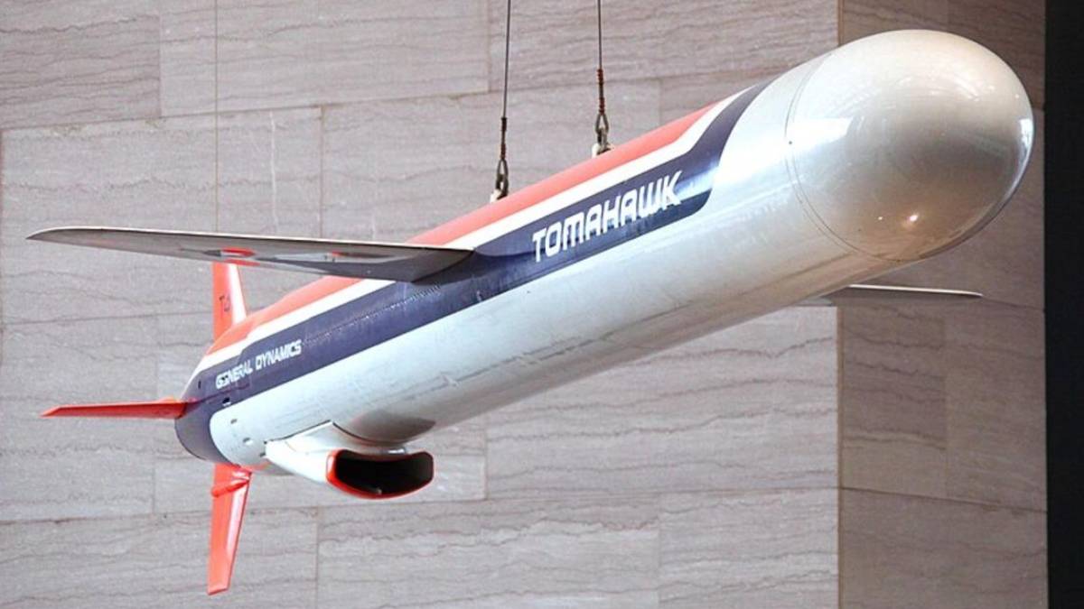 Hanging display model of a Tomahawk aircraft with red, white, and blue livery labeled Tomahawk and General Dynamics, suspended from cables against a stone wall
