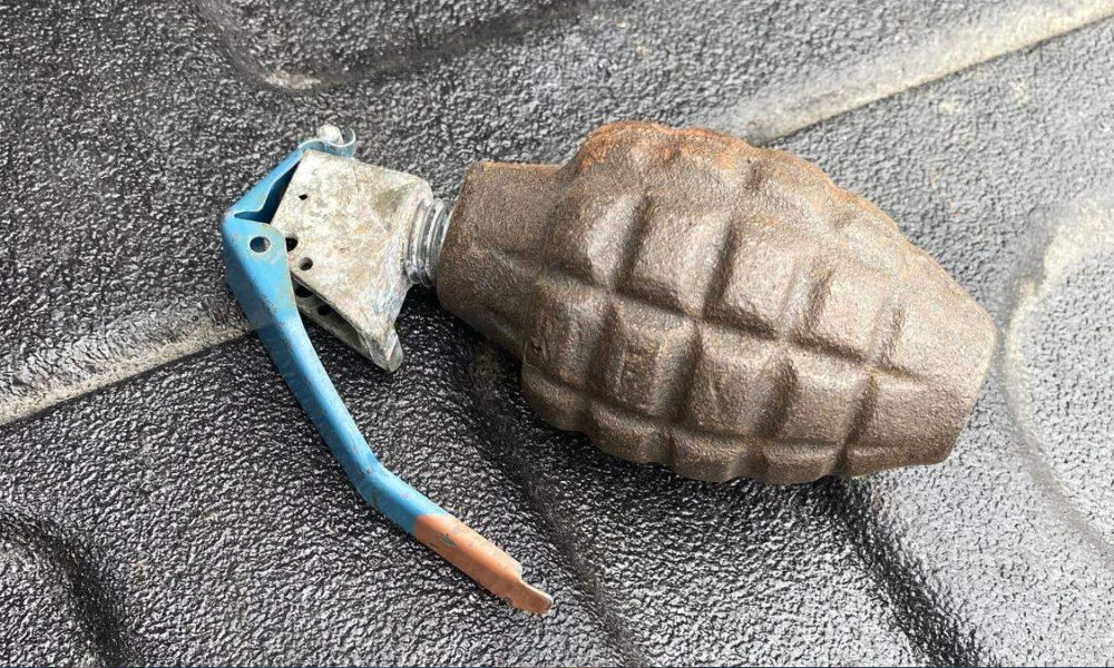 Rusty hand grenade with a blue safety lever resting on a dark textured surface.