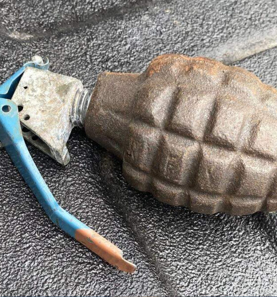 Rusty hand grenade with a blue safety lever resting on a dark textured surface.