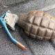 Rusty hand grenade with a blue safety lever resting on a dark textured surface.