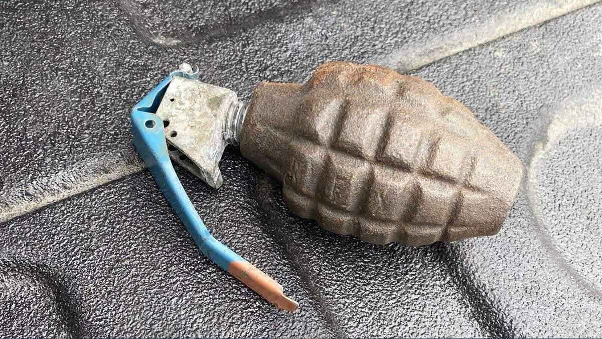 Rusty hand grenade with a blue safety lever resting on a dark textured surface.
