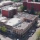 Aerial view of a small downtown block with brick buildings, trees, and parked cars along intersecting streets. Red brick building stands out in the center-right.
