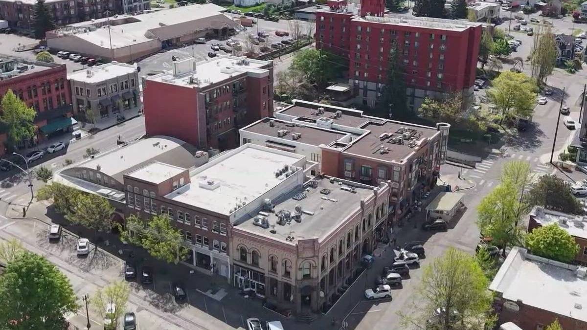 Aerial view of a small downtown block with brick buildings, trees, and parked cars along intersecting streets. Red brick building stands out in the center-right.