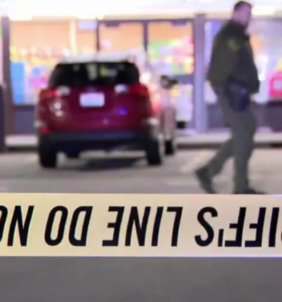 Crime scene tape in the foreground reads 'DO NOT CROSS' (inverted); blurred man and a red SUV seen near a storefront.