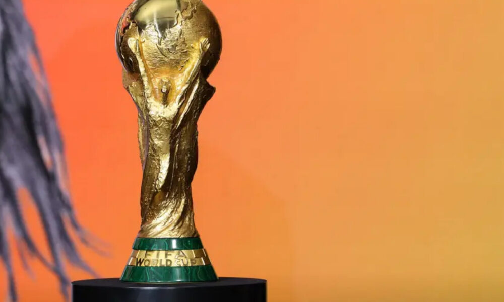 FIFA World Cup trophy in gold on a black pedestal against an orange gradient background.