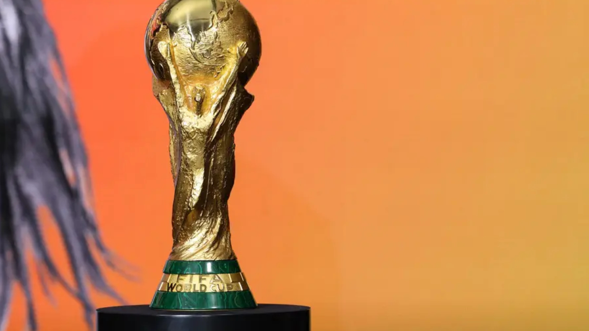 FIFA World Cup trophy in gold on a black pedestal against an orange gradient background.