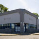 Front view of a Rite Aid store with gray facade, blue-framed windows, and a closed handicap curb; empty parking lot under a clear sky.