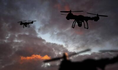 Two quadcopter drones silhouetted against a cloudy sunset sky, flying in formation.