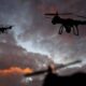 Two quadcopter drones silhouetted against a cloudy sunset sky, flying in formation.