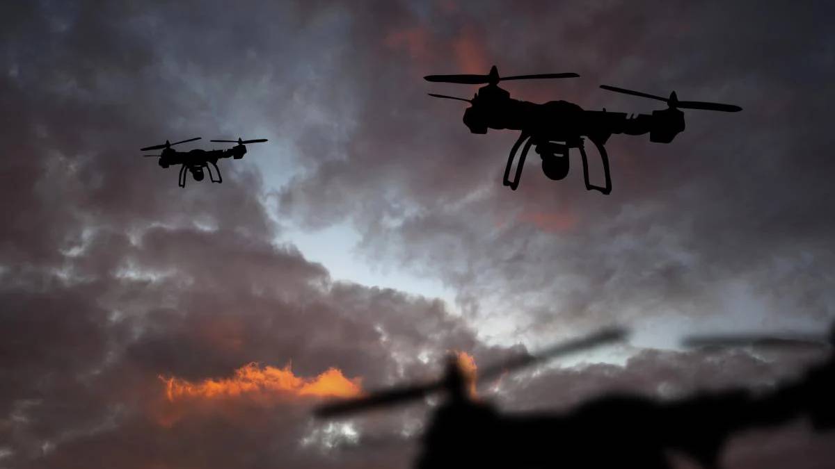 Two quadcopter drones silhouetted against a cloudy sunset sky, flying in formation.