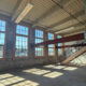 Sunlit industrial loft with brick walls, tall sash windows, and a metal staircase to a mezzanine.