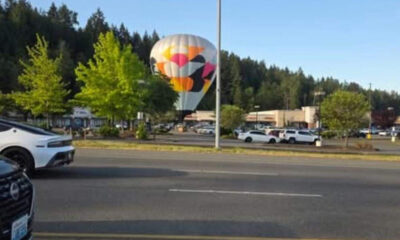 Colorful hot-air balloon sculpture in a shopping-center parking lot, with cars and green trees in the background.
