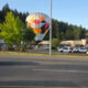 Colorful hot-air balloon sculpture in a shopping-center parking lot, with cars and green trees in the background.