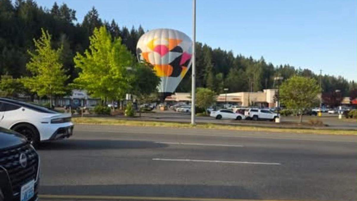 Colorful hot-air balloon sculpture in a shopping-center parking lot, with cars and green trees in the background.