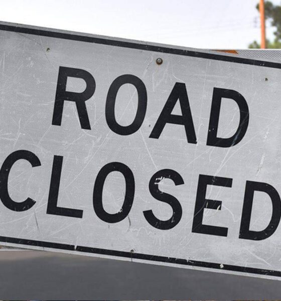 Road closed sign mounted on striped barrier blocking a street roadwork scene