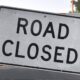 Road closed sign mounted on striped barrier blocking a street roadwork scene