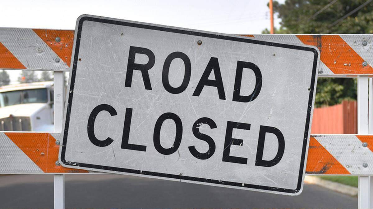 Road closed sign mounted on striped barrier blocking a street roadwork scene