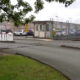 Railroad crossing barriers in front of a gated industrial parking lot with a security booth and fenced perimeter.